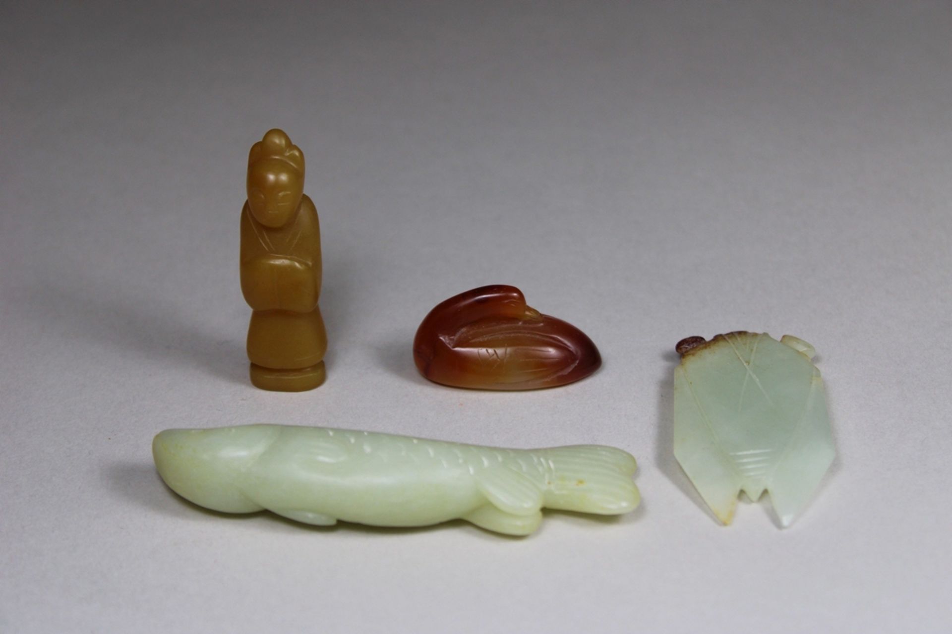 Vier Schnitzereien, China, 1 Beamter aus gelben Jade, H.: 5,5 cm, 1 Ente aus Rote-Achat, L.: 3,9 cm