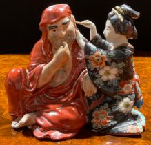 A Japanese porcelain figure group, as a seated robed monk with Geisha attendant cleansing his ear,