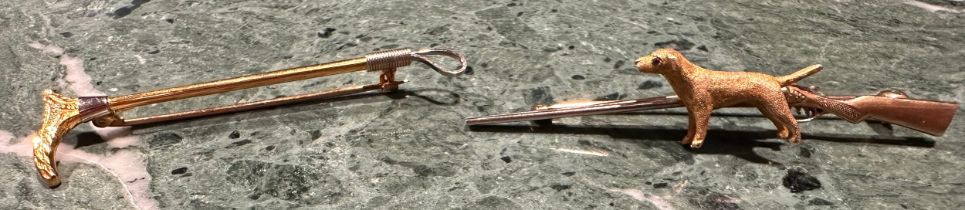 A gold coloured metal bar brooch as a rifle with gun dog to fore, ruby chip eye, stamped '9ct' for