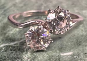 A two-stone diamond cross-over ring, the two round brilliant cut stones claw set, each approximately