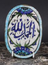 A Middle Eastern oval tile, painted in the Iznik palette with stylised flowers and inscribed with