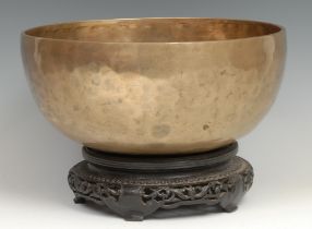 A Tibetan bronze singing bowl, feint inlaid inscription, 27cm diam, pierced and carved hardwood