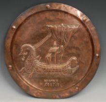 An Arts and Crafts copper circular charger, repousse chased with a drakkar longship titled Norman
