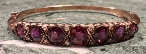 A ruby and diamond hinged bangle, the seven graduated oval facet cut stones divided by pairs of