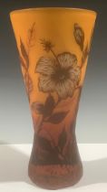 A cameo glass waisted cylindrical vase, with leafy flowers in shades of red on an orange ground,