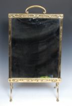 An Art Nouveau brass fire screen, arched handle, mirrored banner, the frieze and apron embossed with