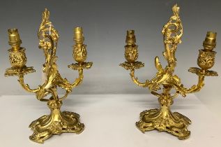 A pair of ornate cast iron two branch candelabras, gilt, the crest a scrolling acanthus, terminating