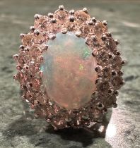 An opal and diamond cluster ring, central oval opal flashing green, red, orange and violet colour