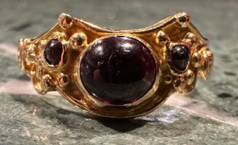 An 18ct gold garnet ring, set with three oval and circular cabochon red garnets, shaped scrolling