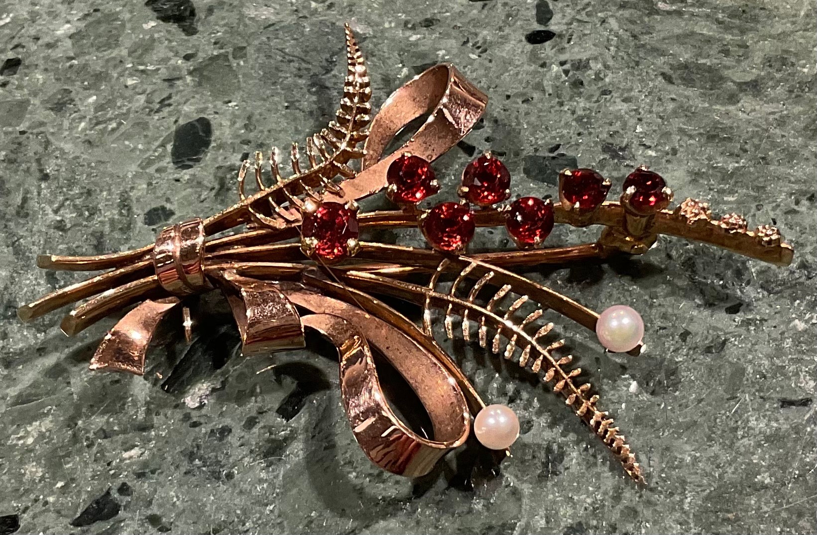 A 9ct gold garnet and seed pearl brooch, cast as a spray of ribbon tied ferns and budding stems, the