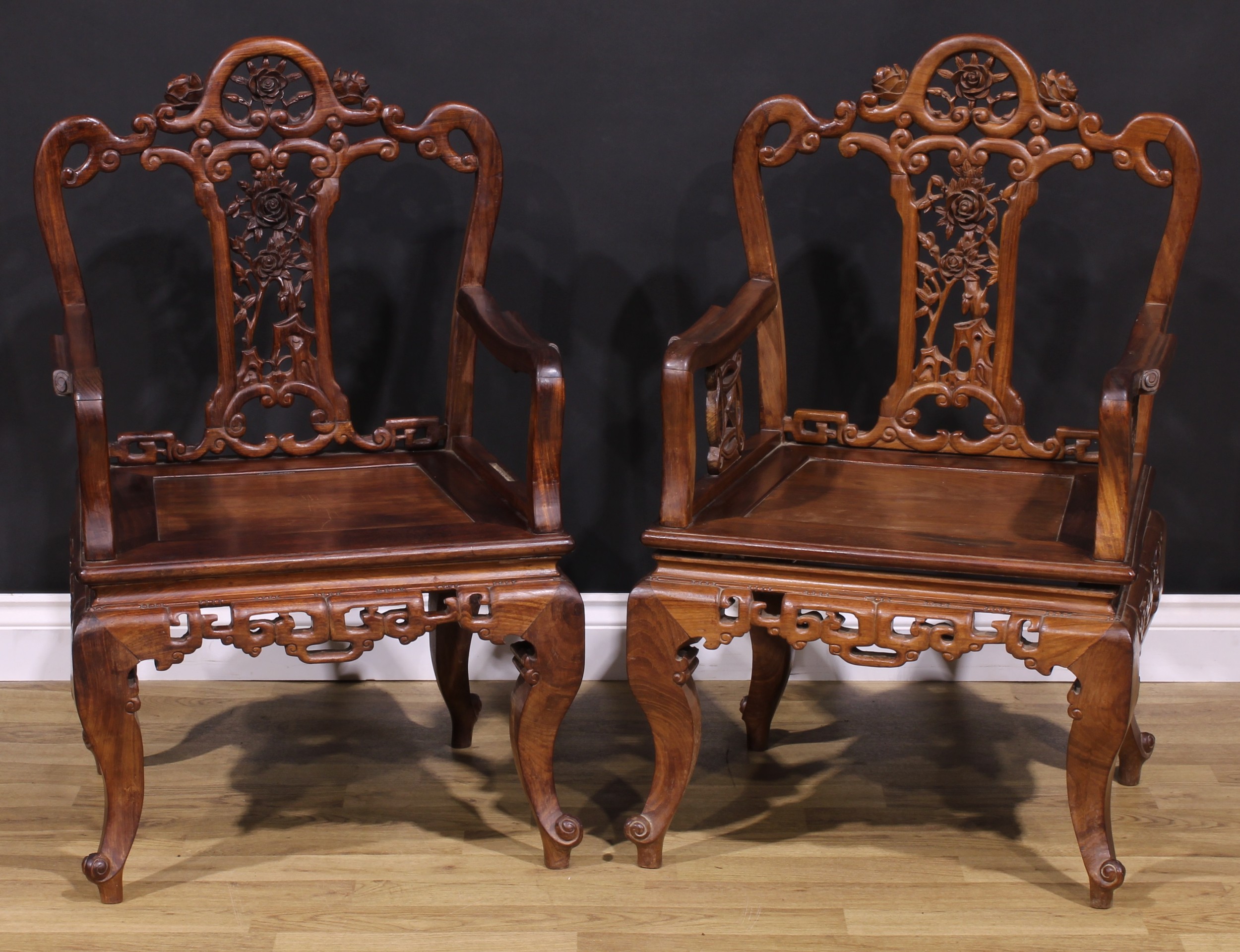 A pair of Chinese hardwood armchairs, each with a shaped back pierced and carved with scrolls and