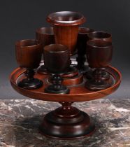 Treen - a George III turned pedestal egg cruet, with six egg cups, the stand 19cm diam, early 19th