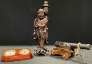 A Chinese carved hardwood figural lamp; a desk cannon; a mahogany and brass desk top combination