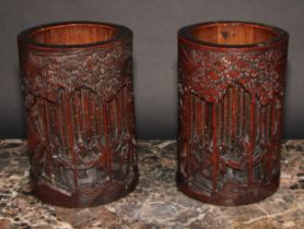 A pair of Chinese bamboo bitong brush pots, carved with figures amongst trees, 18.5cm high, early