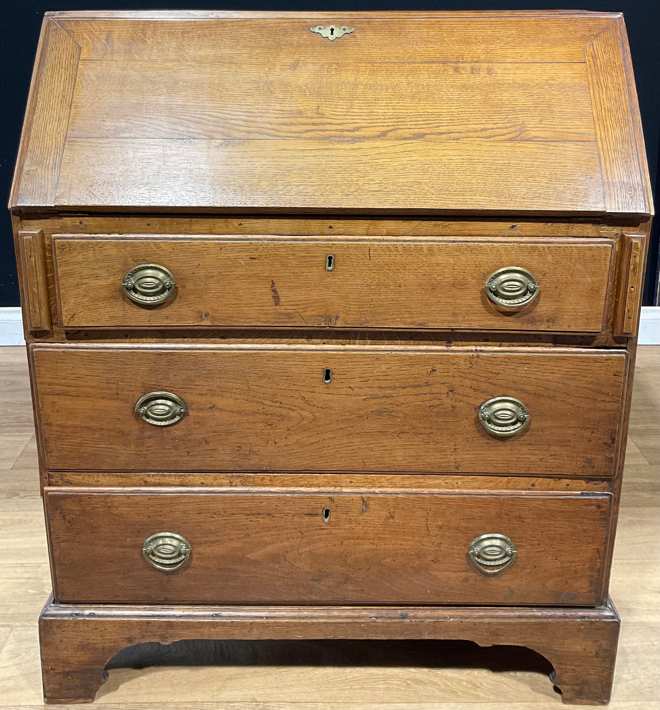 A George III oak bureau, fall front enclosing small drawers and pigeonholes, above three long