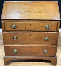 A George III oak bureau, fall front enclosing small drawers and pigeonholes, above three long