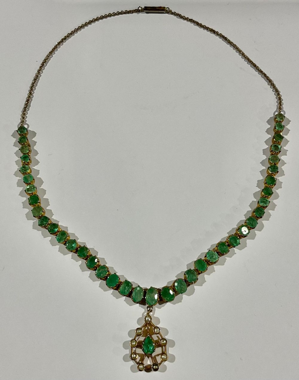 A gold plated necklace, set with a strand of graduated faceted oval emeralds, suspended with a