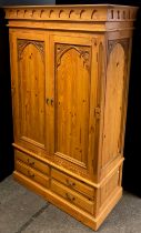 A Gothic style pine double wardrobe, having a pair of doors with Gothic arch carved panels, above