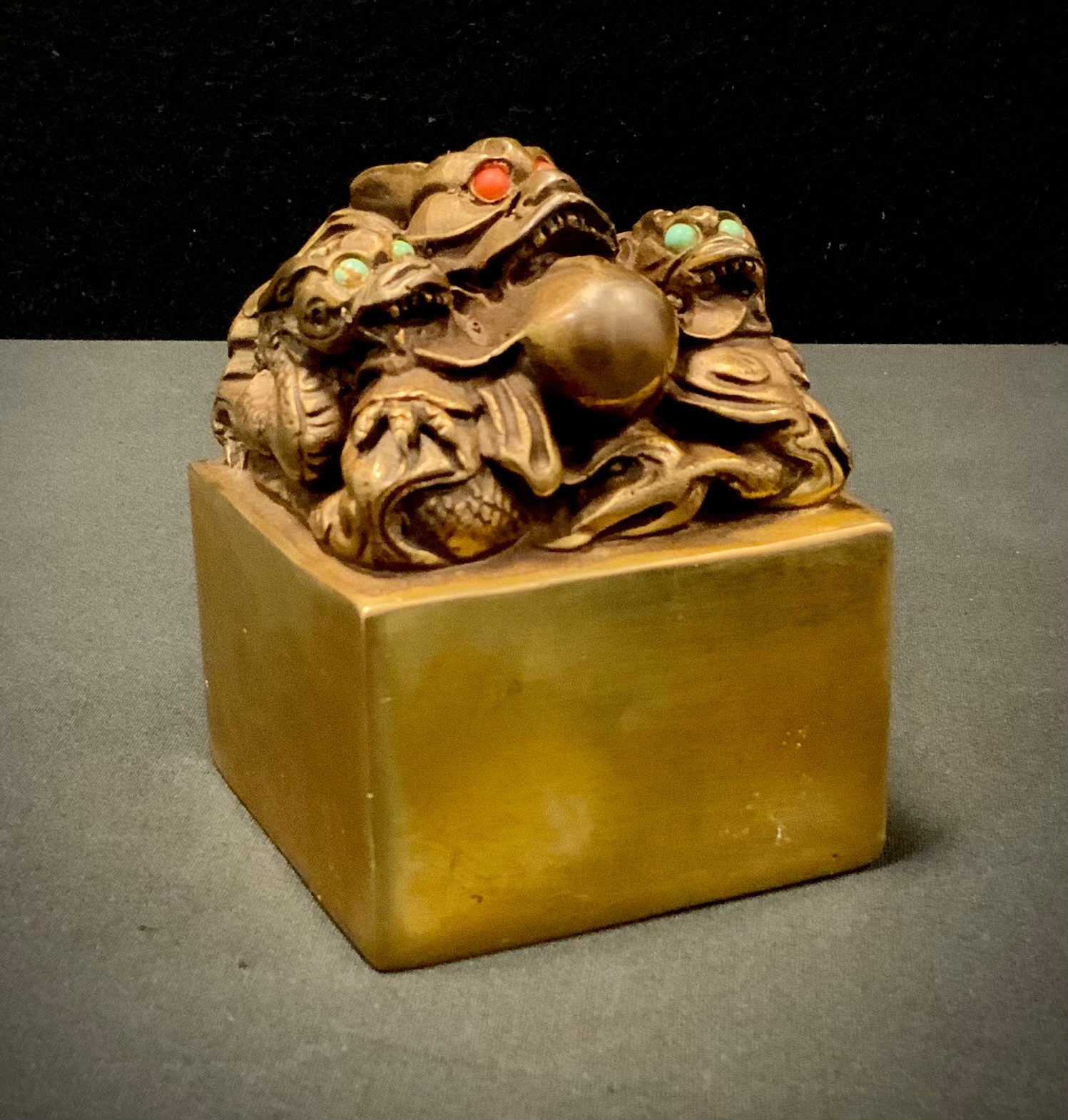 A Gilt bronzed metal Chinese dragon seal, with green and red cabochon eyes, approx 10cm x 7cm.