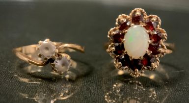 An oval opal and red garnet cluster ring, creamy white opal cabochon surrounded by ten round deep