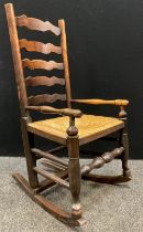 A George III elm ladder-back rocking chair, of small proportions, rush seat, 95.5cm high x 51cm wide