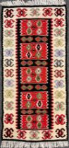 A Turkish Kilim rug, hand-knotted with abstract motifs, in tones of red, black, blue, green, and
