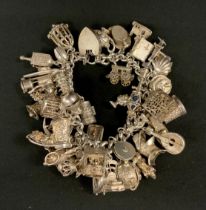 A large silver charm bracelet suspending over forty charms inc Miners Lamp, Moon with American