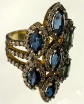 An Edwardian style diamond and sapphire multi panel cluster ring, composed of seven navette clusters