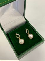 A pair of diamond and cultured pearl drop earrings, diamond accented flame bales with creamy