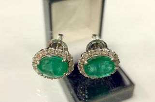 A pair of emerald and diamond cluster earrings, each with a central oval emerald surrounded by