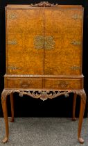 A burr walnut cocktail cabinet, carved cresting above pair of doors enclosing mirrored interior.