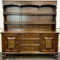 An oak dresser, plate rack top with two tiers of shelving, over a base with pair of carved panel