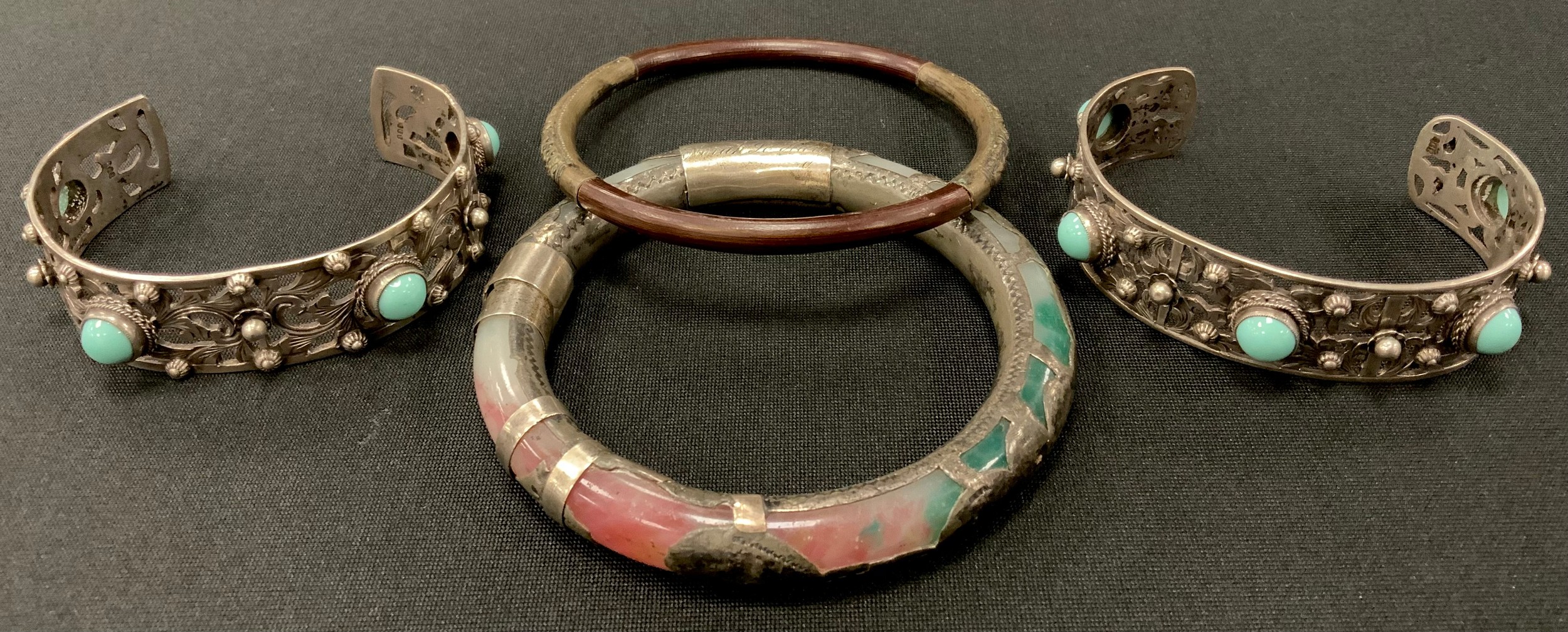 A Chinese white metal and multi tone stone possibly jade bangle, showing opaque tones of green,