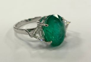 An emerald and diamond ring, central oval emerald approx 5.63ct, between trilliant cut diamond