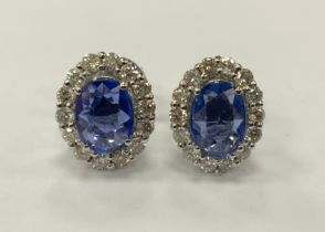 A pair of sapphire and diamond oval stud earrings, central mid blue oval sapphire within halo of
