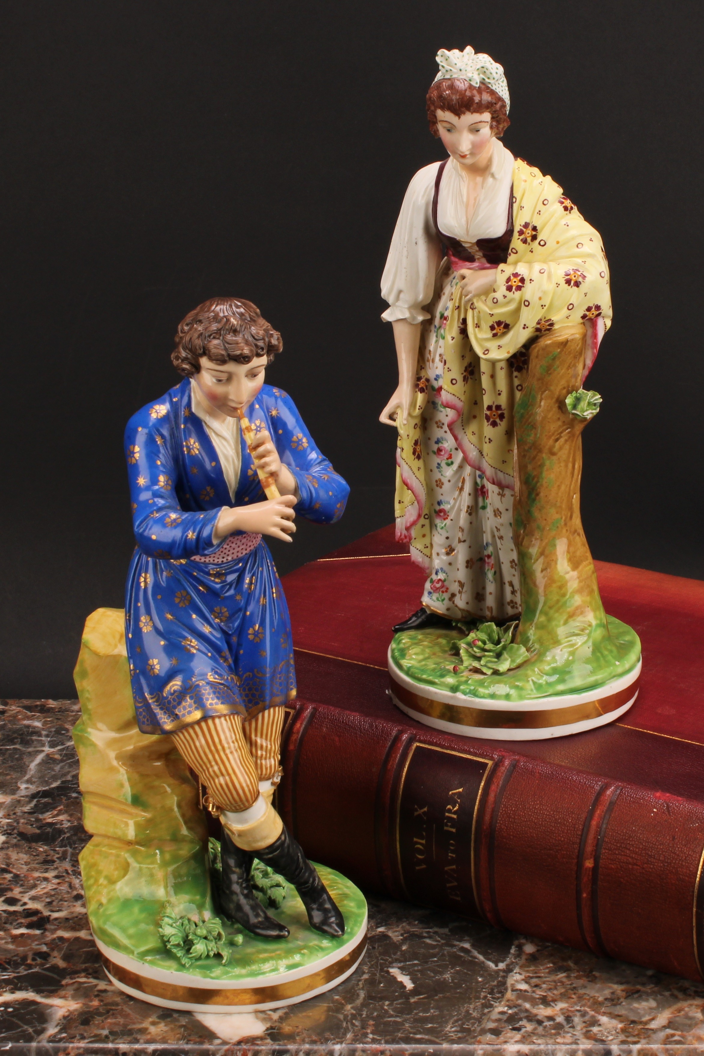 A pair of Bloor Derby figures, of a musician and his companion, he seated on rocky outcrop playing