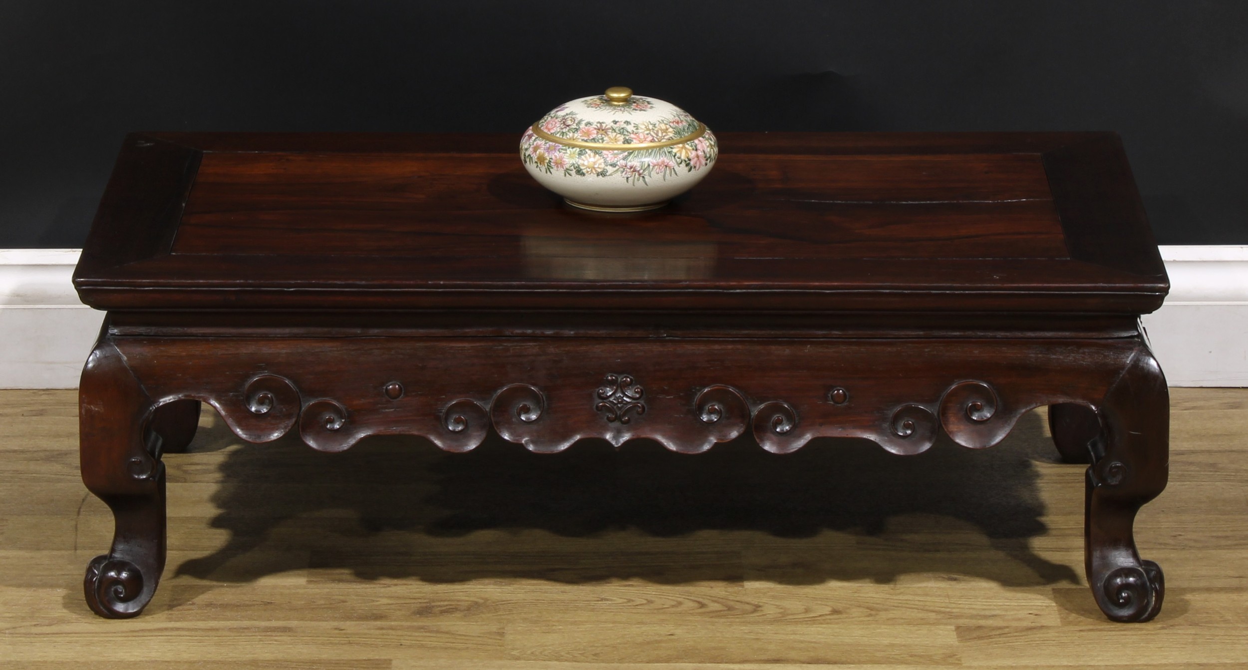A Chinese hardwood low tea or kang table, rectangular panel top, shaped apron carved with stylised