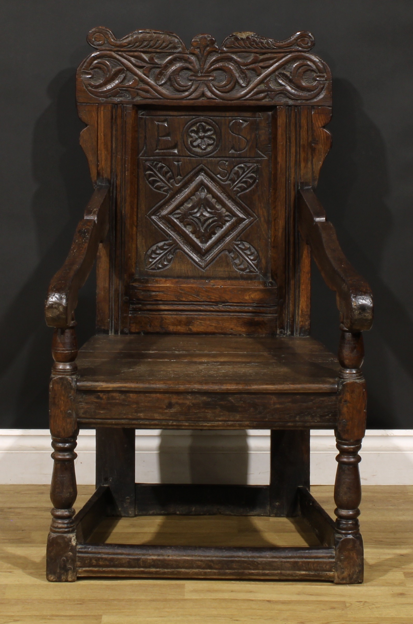 A 17th century oak wainscot armchair, shaped cresting carved with scrolling leafy branches, the
