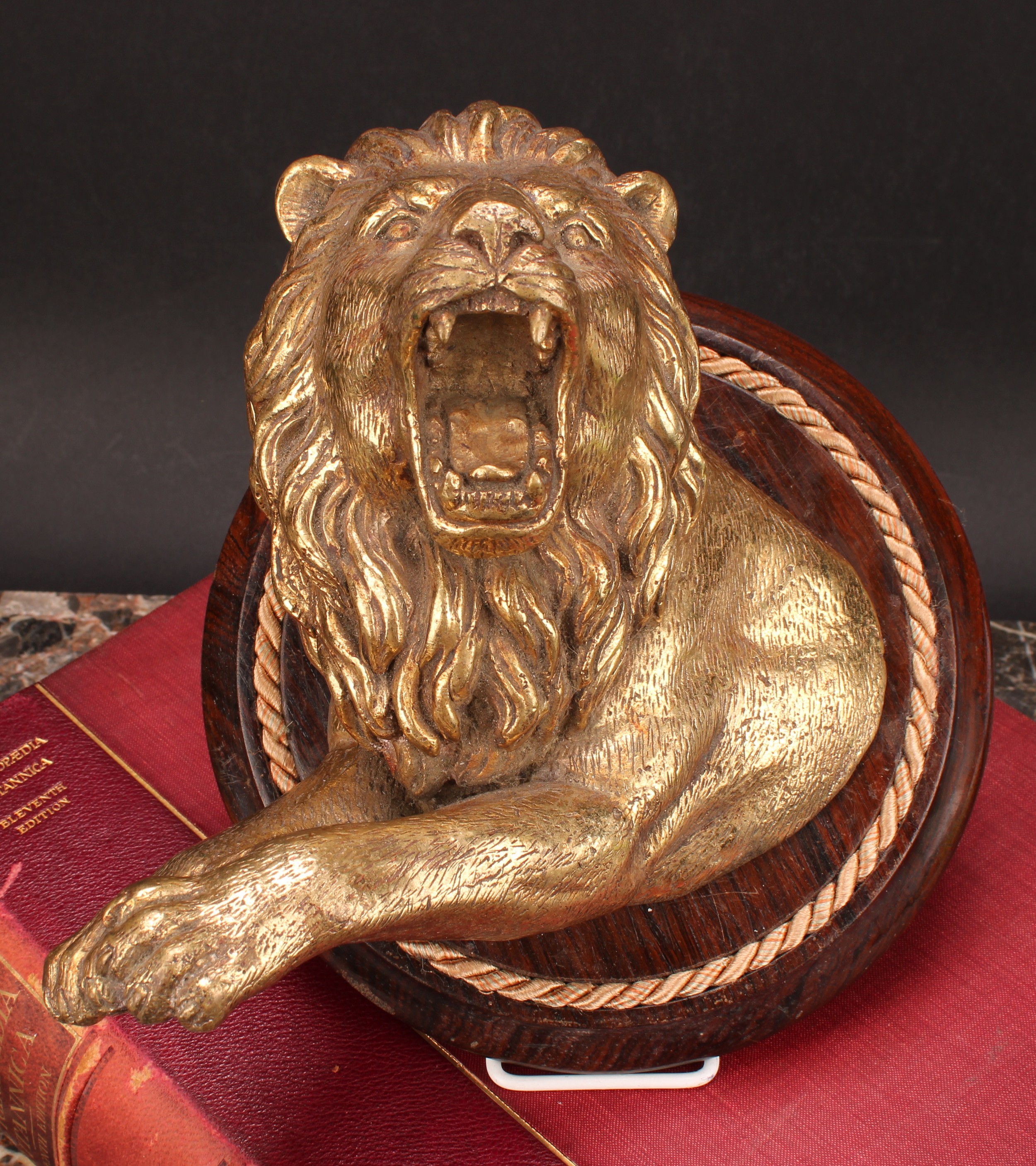 A 19th century gilt metal wall plaque, boldly cast as a ferocious lion, circular rosewood mount,