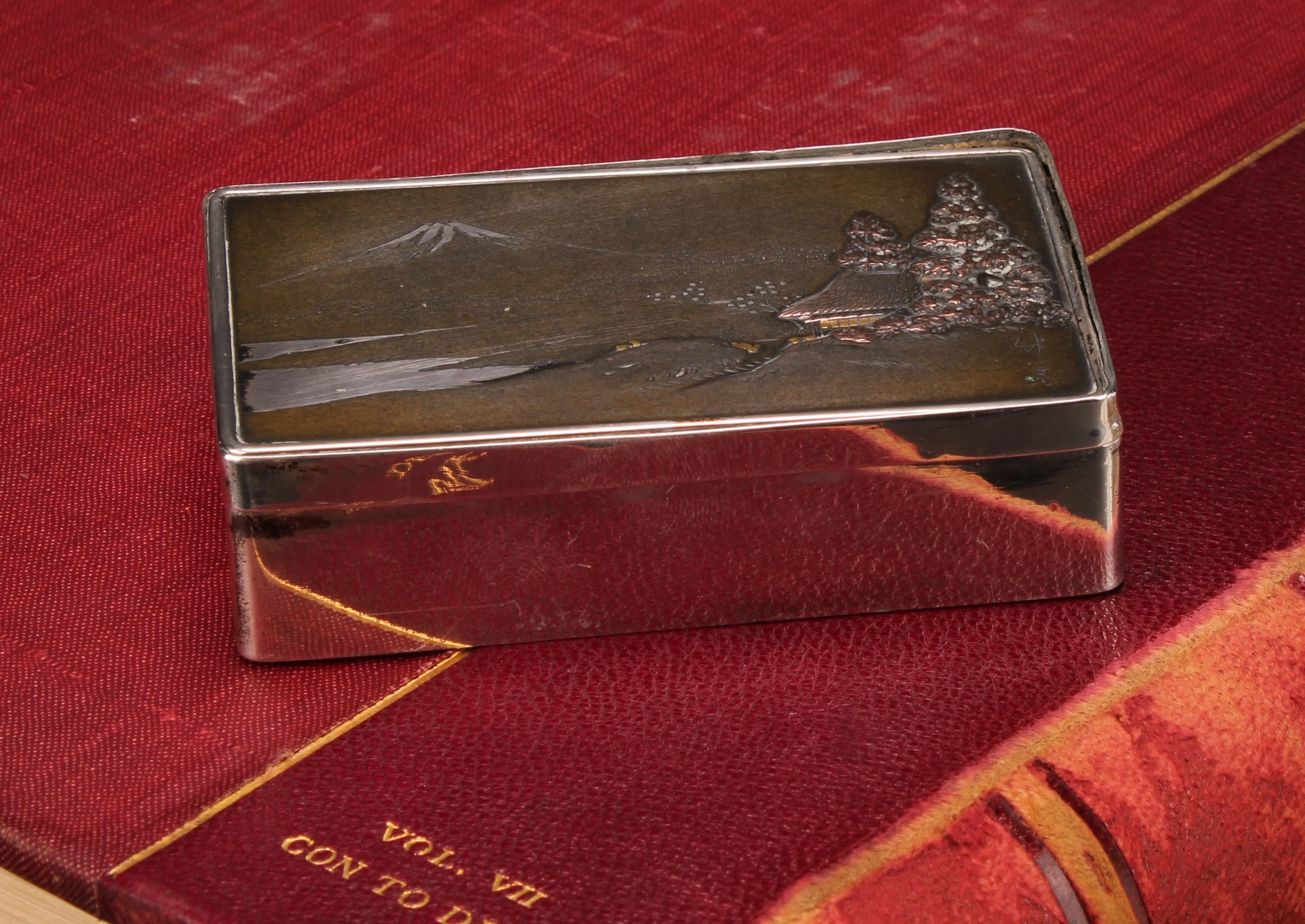 A Japanese silver and mixed metal rounded rectangular snuff box, the hinged cover decorated with