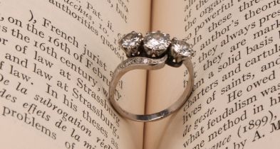 A diamond and platinum three stone twist ring, the central round brilliant cut stone flanked by