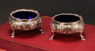A pair of Victorian silver cauldron salts, chased with flowers and leaves, shell feet, blue glass