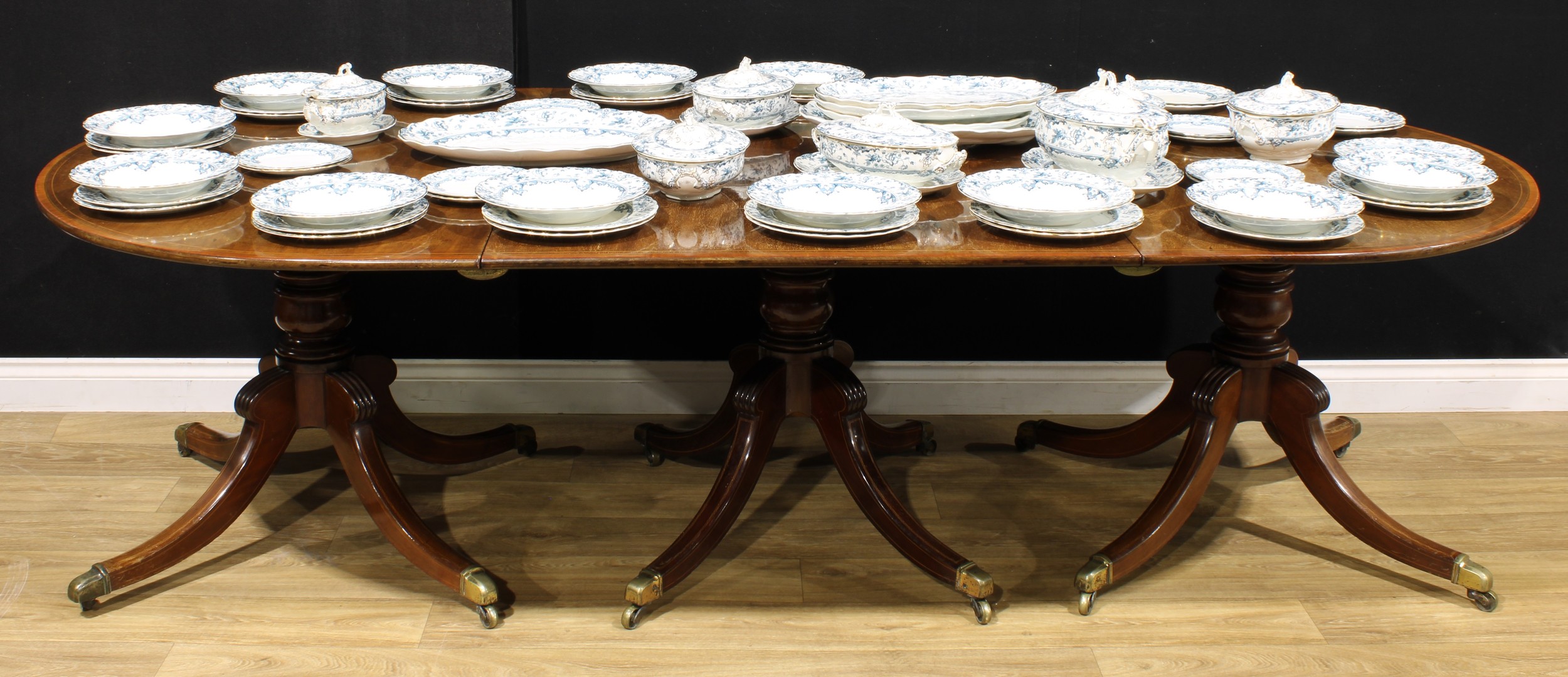 A Post-Regency mahogany triple-pillar dining table, each tilting top crossbanded with satinwood