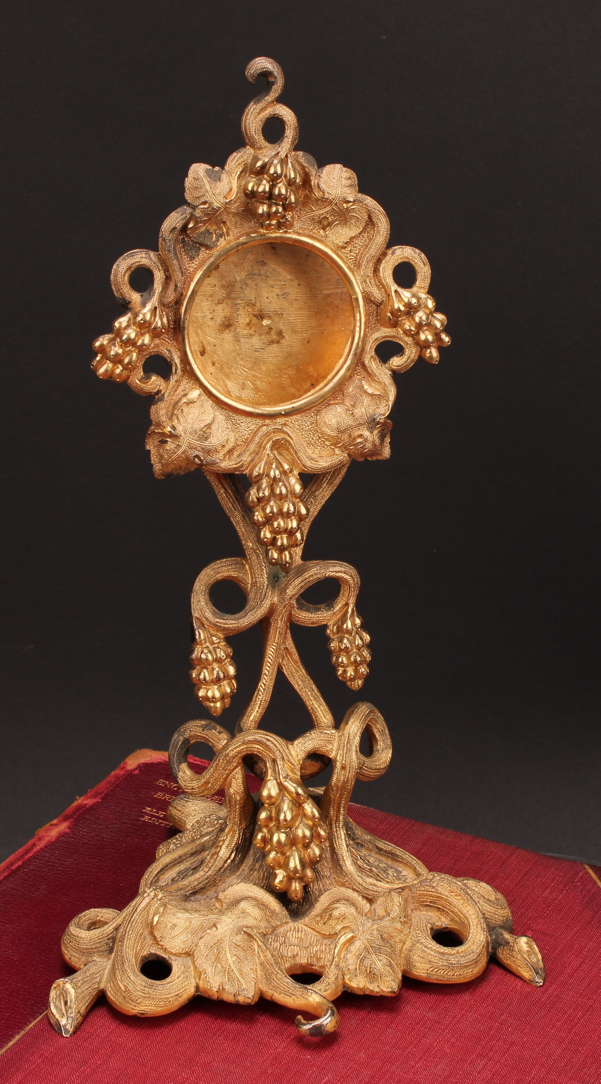 An early 20th century gilt metal pocket watch stand, cast throughout with fruiting vine, triform