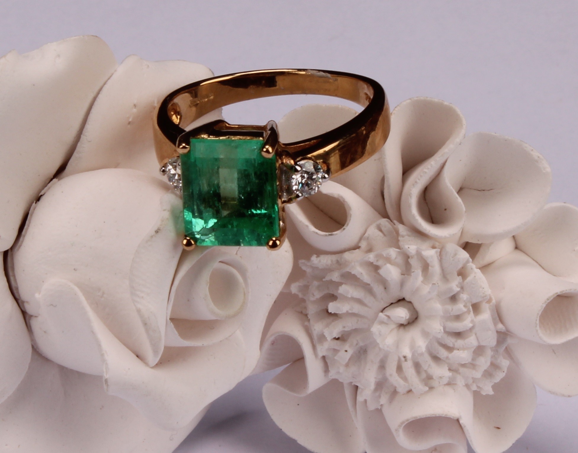 An 18ct gold, emerald and diamond ring, central cushion cut stone