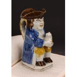 An early 19th century Prattware Toby jug, seated holding a jug of foaming ale, painted in polychrome