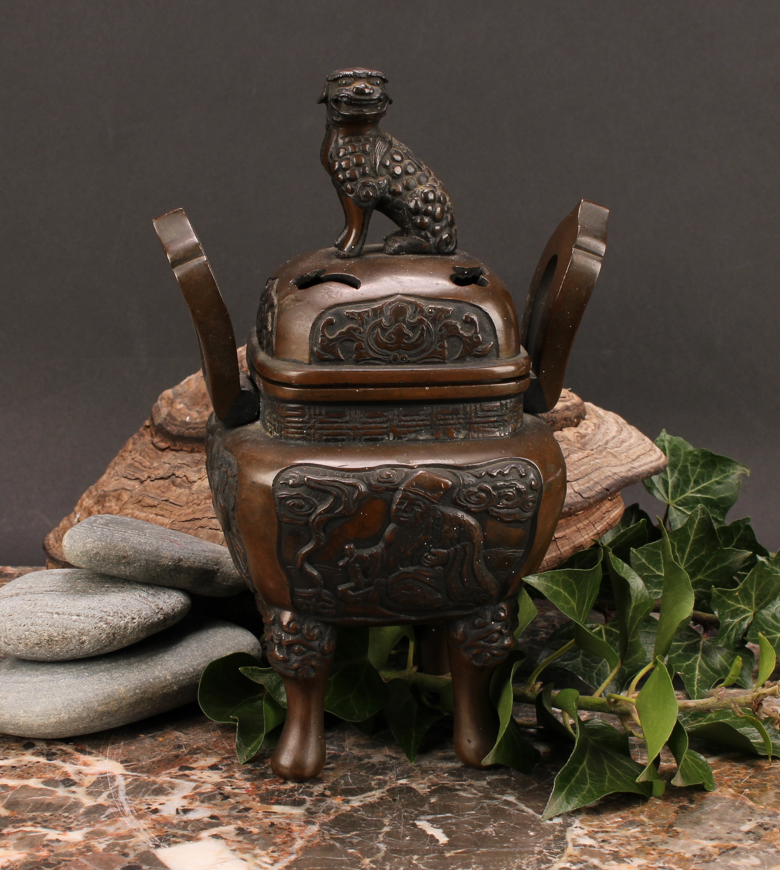 A Chinese bronze censer and cover, surmounted by a temple lion, cast with scholars, shaped loop