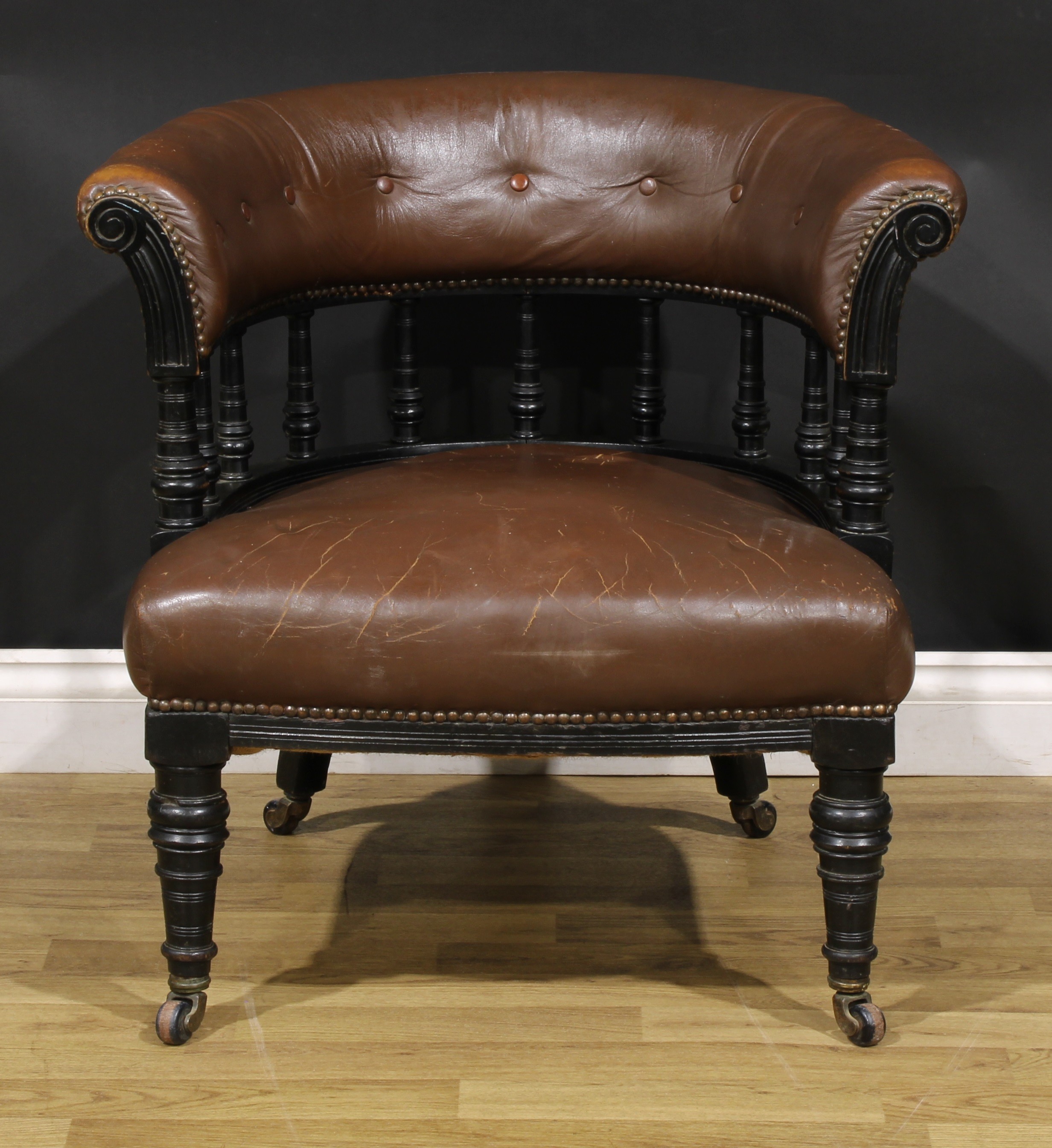 A late Victorian ebonised club or library chair, stuffed-over upholstery, turned forelegs, 69cm
