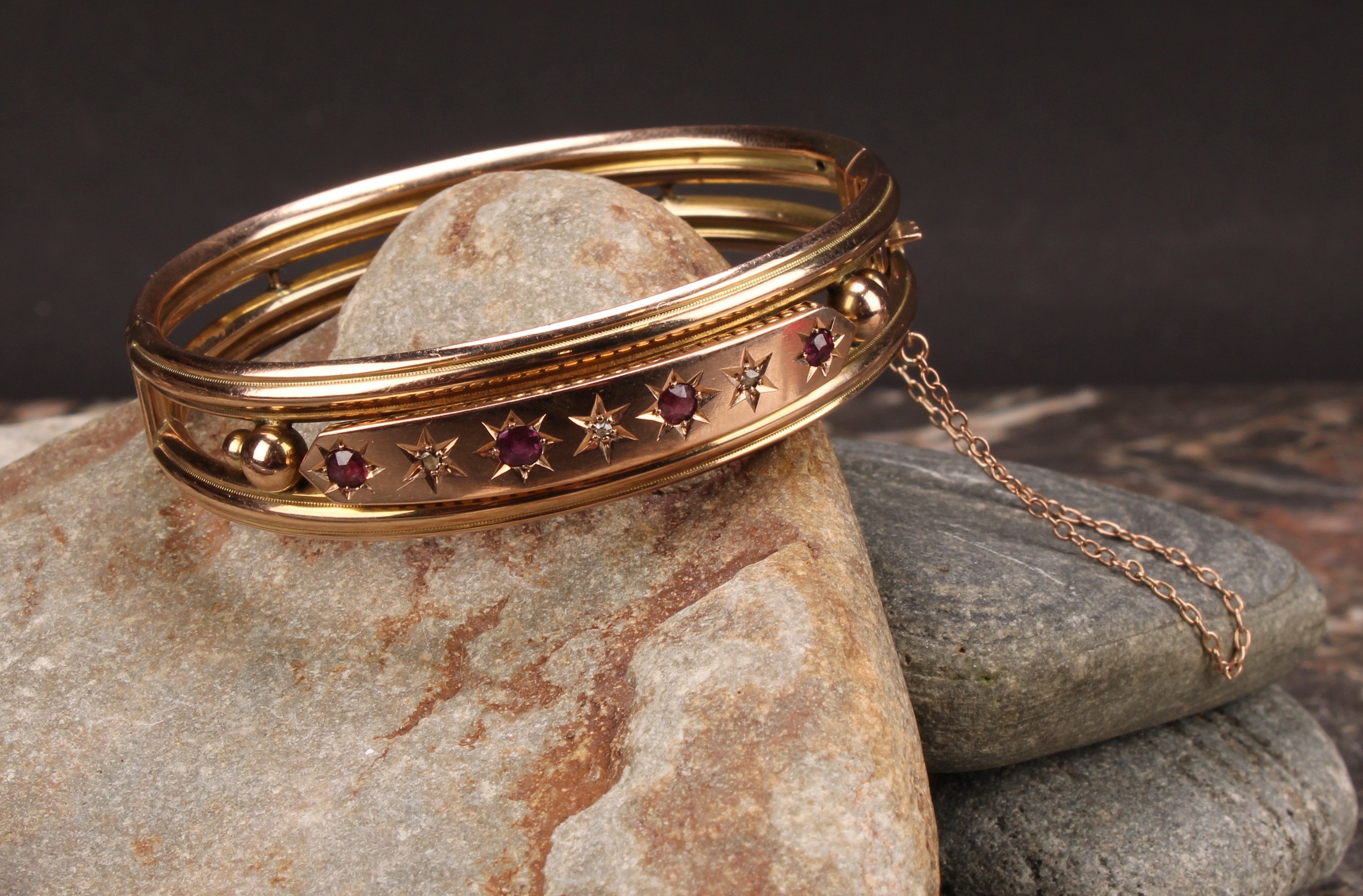 An Edwardian ruby and diamond 9ct gold hinge bangle, set with four old cut pinky red rubies, each