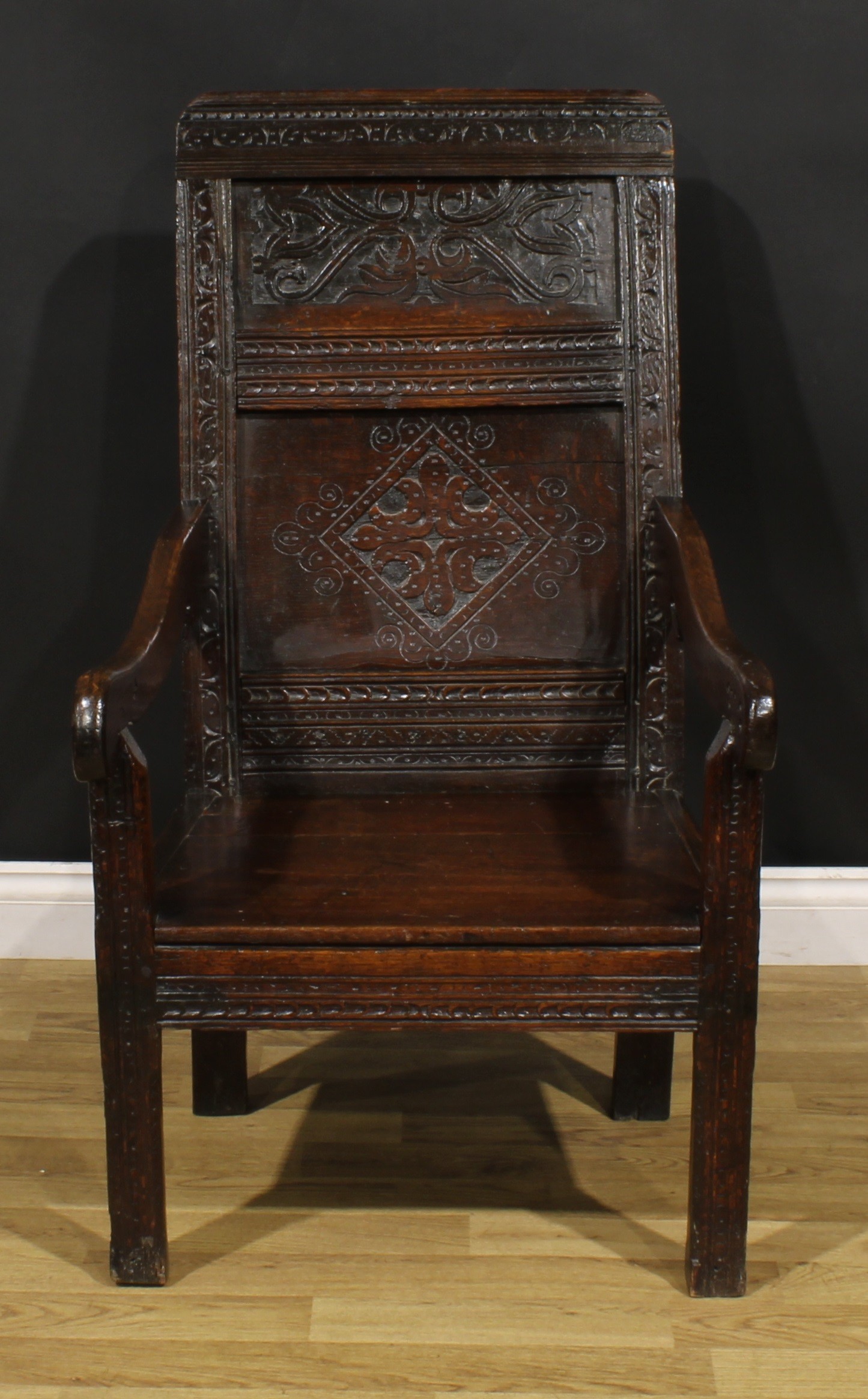 A 17th century oak wainscot armchair, rectangular panel back carved with lozenges and leafy scrolls,